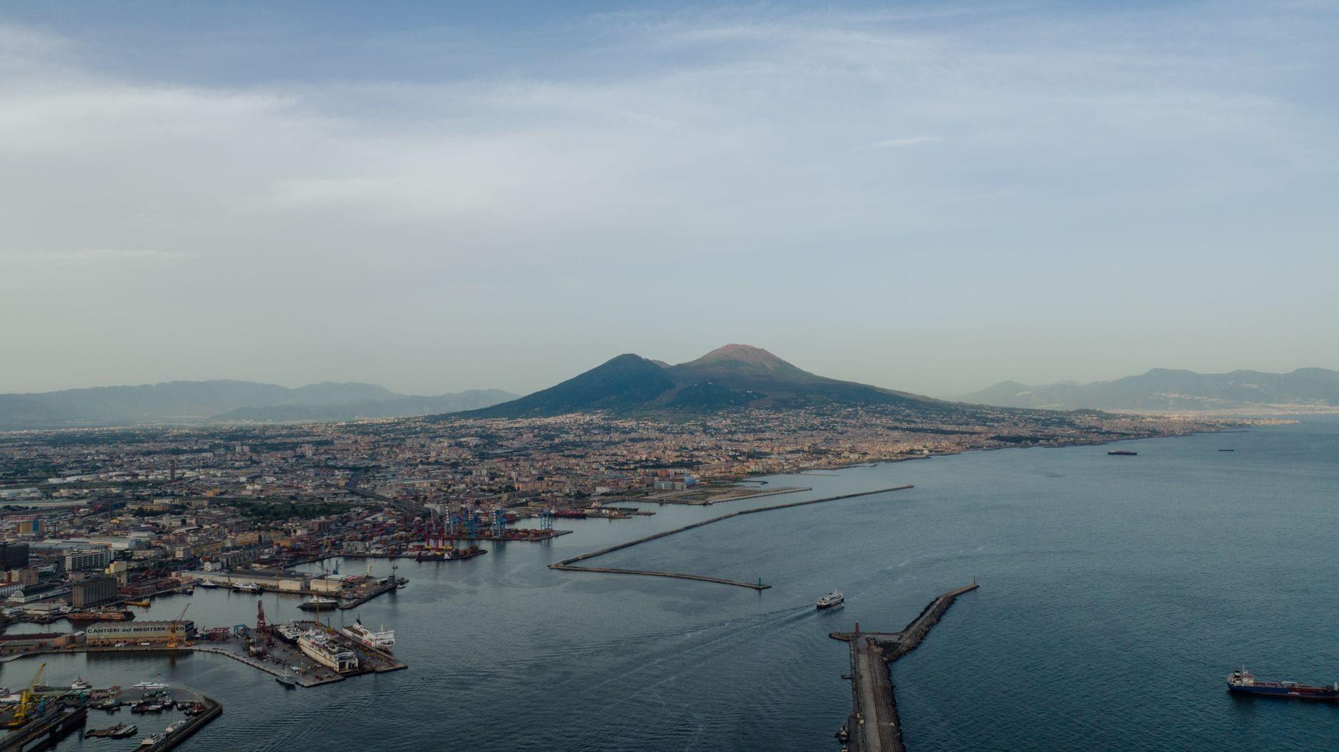 Panoramic aerial view of Mount Vesuvius rising above the Gulf of Naples and coastal cityscape.