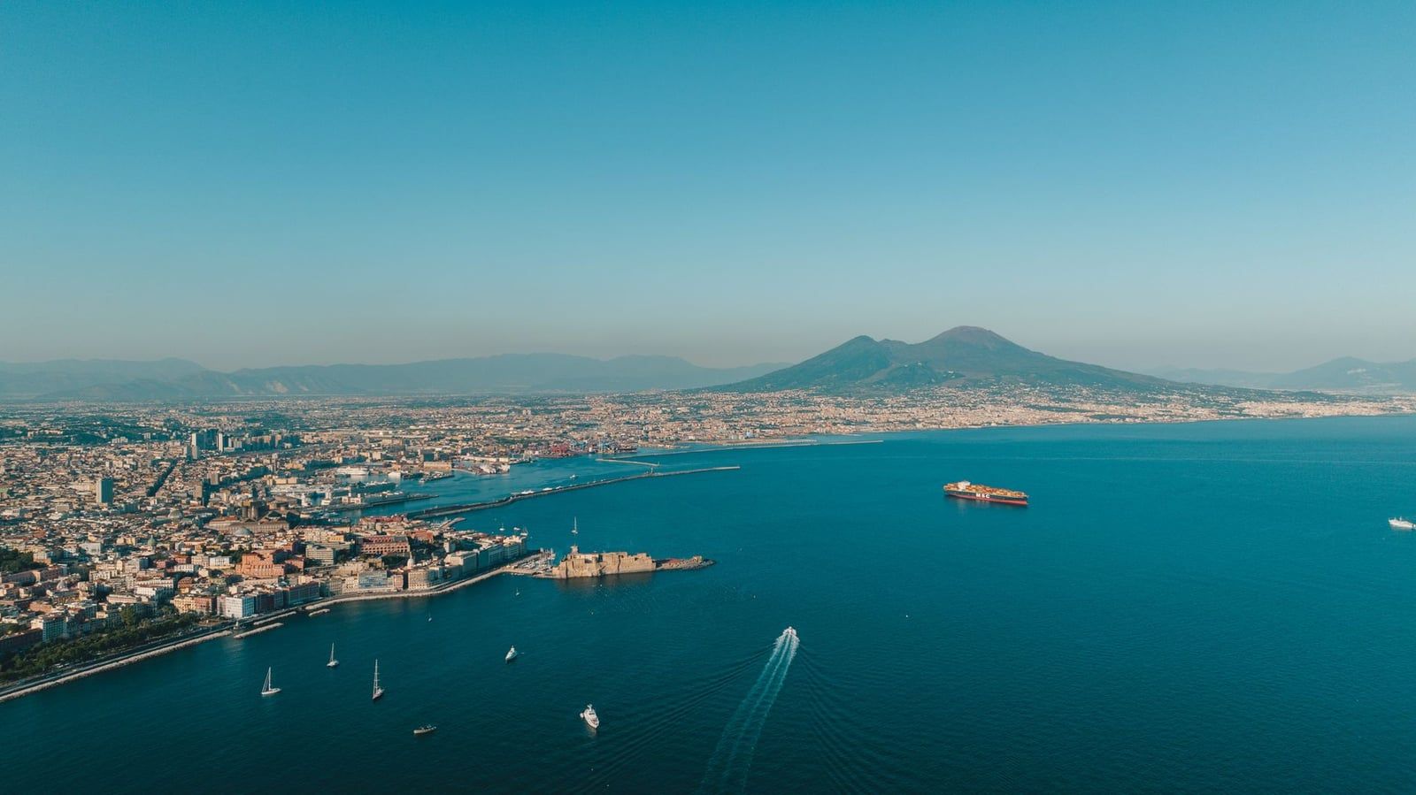 Aerial panoramic view of the Bay of Naples and Castel dell'Ovo with Mount Vesuvius in the background.