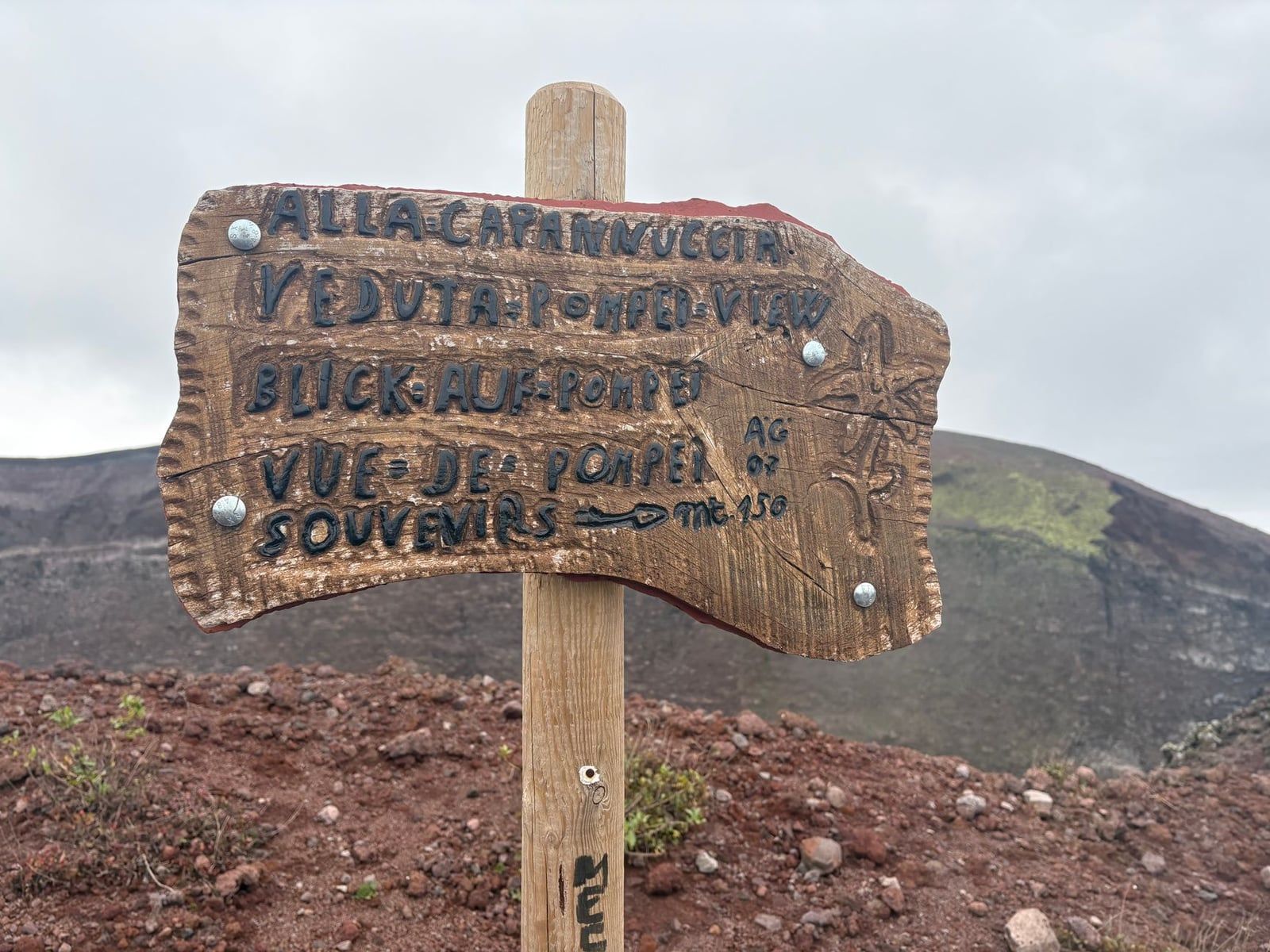 A wooden trail sign on Mount Vesuvius directs visitors toward a Pompeii viewpoint and the Capannuccia hut.